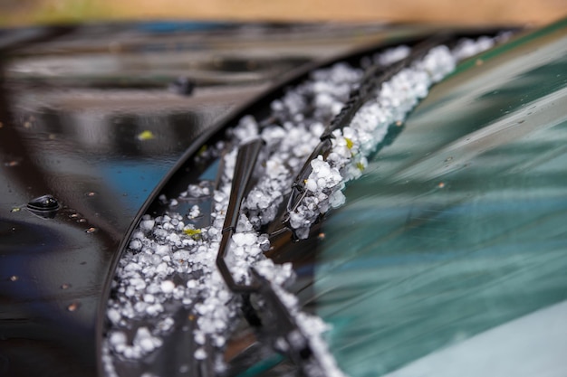 Piccole palline di ghiaccio di grandine sul cofano nero dell'auto dopo un forte temporale estivo in primo piano con messa a fuoco selettiva