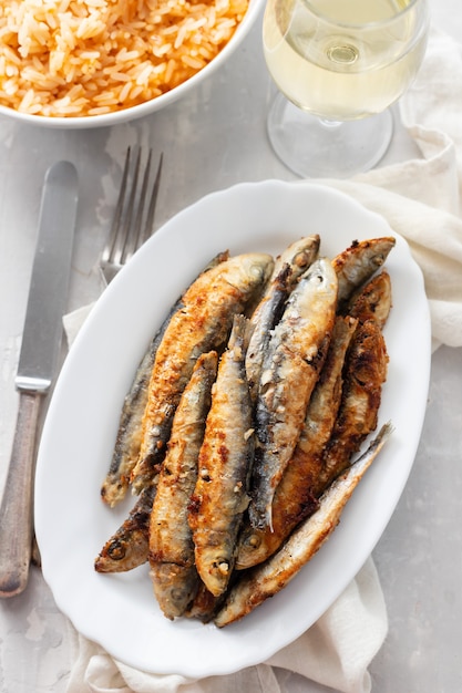 Piccole sarde fritte con riso al pomodoro sul piatto bianco su fondo in ceramica