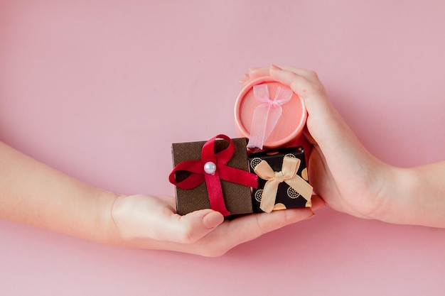 Piccole scatole regalo nelle mani delle donne su sfondo rosa Concetto festivo per San Valentino Festa della mamma o compleanno
