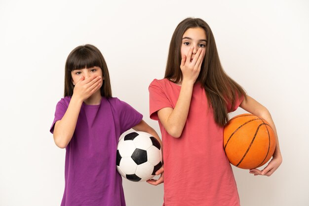 Piccole sorelle che giocano a calcio e basket isolato su sfondo bianco che copre la bocca con le mani per dire qualcosa di inappropriato