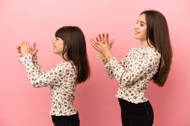 Piccole sorelle ragazze isolate su sfondo rosa che applaude dopo la presentazione in una conferenza