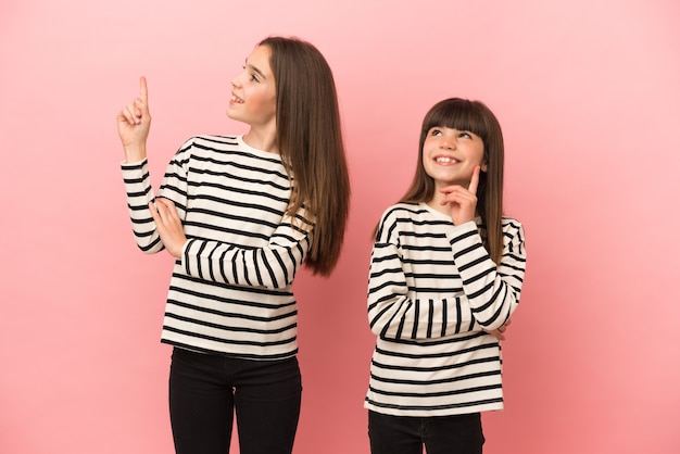 Piccole sorelle ragazze isolate su sfondo rosa che punta una grande idea e alzando lo sguardo