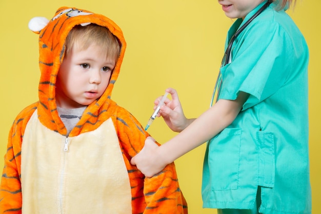 Piccoli bambini caucasici giocano al dottore, una ragazza vestita da medico fa un'iniezione a un ragazzo vestito da tigre