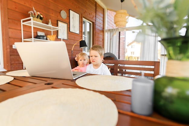 Piccoli bambini sorridenti fratello e sorella ridono e giocano al laptop, comunicano in chat in videoconferenza Interni domestici spaziosi e accoglienti.