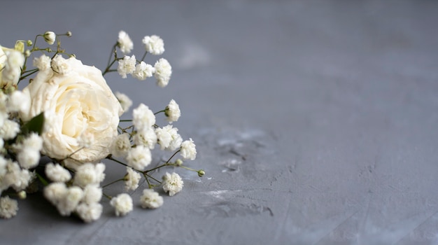 Piccoli fiori bianchi e rose bianche giacciono su uno sfondo di cemento grigio. Bandiera. Posto per il testo.