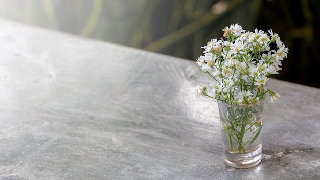 Piccoli fiori bianchi in un bicchiere su uno sfondo concreto