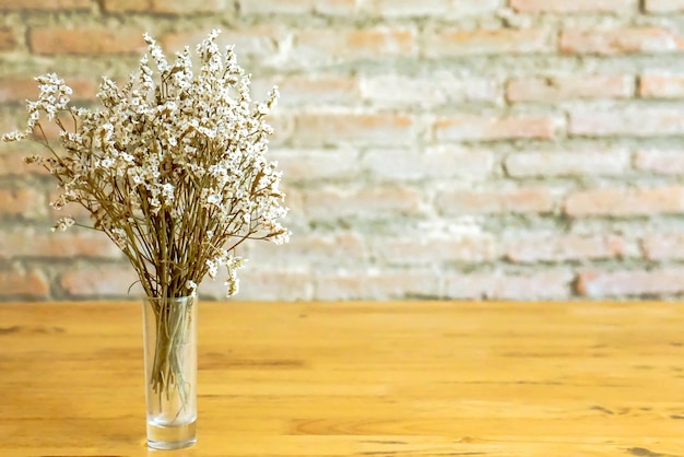 Piccoli fiori bianchi in vaso di vetro sulla tavola di legno