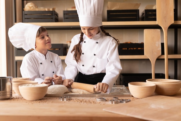 Piccoli fornai che rotolano la pasta sul tavolo