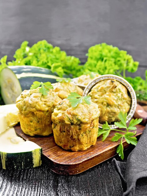 Piccoli muffin al formaggio e zucchine con erbe aromatiche, prezzemolo, timo, coltello e tovagliolo su uno sfondo di tavola di legno