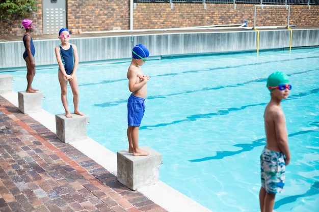 Piccoli nuotatori in piedi sui blocchi di partenza a bordo piscina