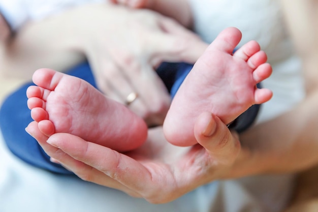 Piccoli piedi e dita del bambino neonato maschio o femmina sulla mano della madre. Madre che tiene in braccio il suo bambino appena nato. Maternità familiare, tenerezza, paternità, concetto di responsabilità.