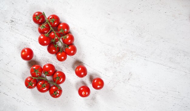 Piccoli pomodori rossi vibranti con viti verdi su pietra bianca come la vista della tavola dall'alto spazio vuoto per il testo a destra