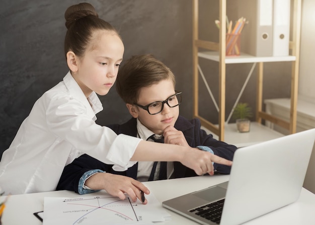 Piccoli professionisti in ufficio. Piccolo ragazzo e ragazza che navigano su laptop, lavoro di squadra, spazio di copia