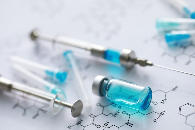 Piccoli vasetti con iniezione e siringa per iniezione su sfondo blu vicino alla formula chimica