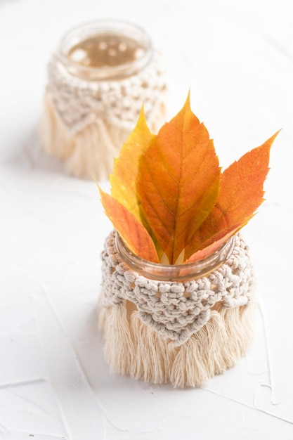 Piccoli vasi in vetro, vasetti, candelieri con copertura in macramè. Foglie d'autunno. boho