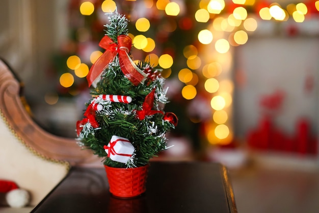 Piccolo albero di Natale artificiale sullo sfondo di ghirlande e albero di Natale gialli luminosi.