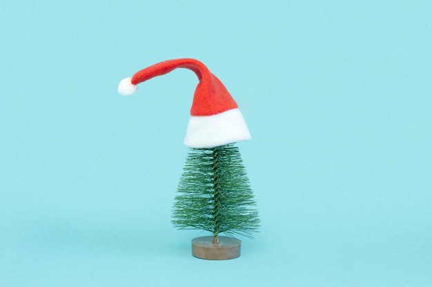 Piccolo albero di Natale in cappelli di Babbo Natale rossi. Decorazione di abete artificiale. Bella imitazione di un mini albero di Natale, con Santa Cap su sfondo blu. Concetto di vacanze di Natale. minimalismo