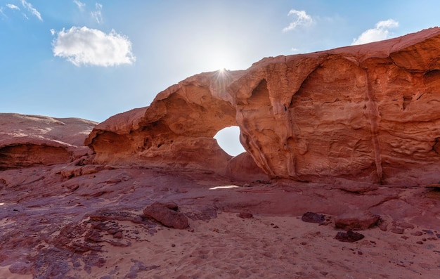 Piccolo arco o piccola formazione di finestre rocciose nel deserto del Wadi Rum, il sole splende su polvere e rocce rosse, cielo blu sopra