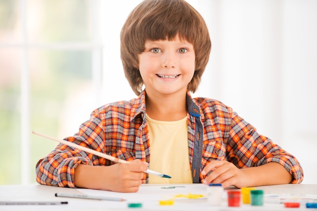 Piccolo artista. Ragazzino felice che si rilassa mentre dipinge con gli acquerelli seduto al tavolo