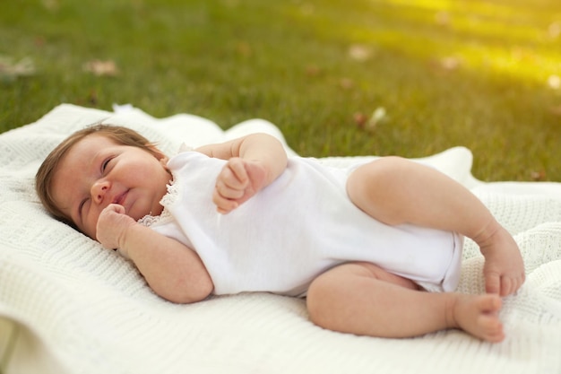 Piccolo bambino affascinante in abiti bianchi sdraiato sulla coperta bianca sull'erba verde