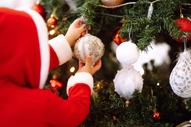 Piccolo bambino appeso palla giocattolo decorativo sul ramo di un albero di Natale.