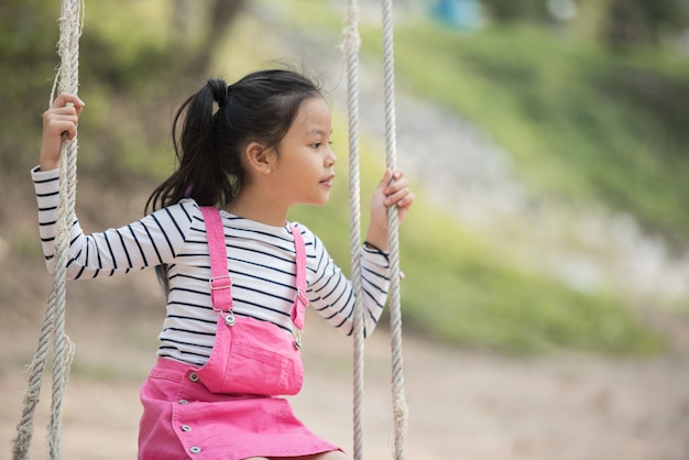 Piccolo bambino asiatico felice della ragazza che si diverte a giocare nel parco giochi nel periodo estivo con il sorriso e la risata sana, adorabile ragazza divertendosi su un'altalena in estate.