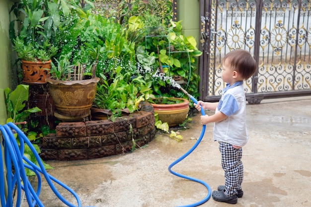 Piccolo bambino asiatico sveglio del neonato del bambino di 2 anni che ha divertimento innaffiando le piante dal tubo flessibile