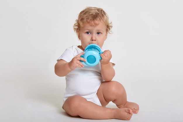 Piccolo bambino beve dalla bottiglia blu