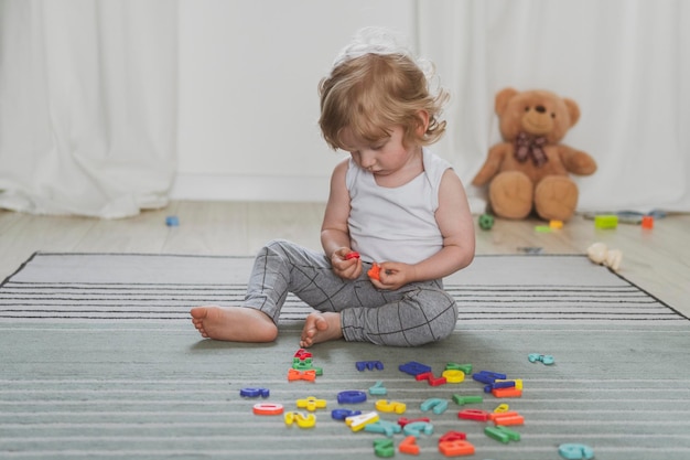 Piccolo bambino carino che gioca con le lettere giocattolo seduto sul pavimento