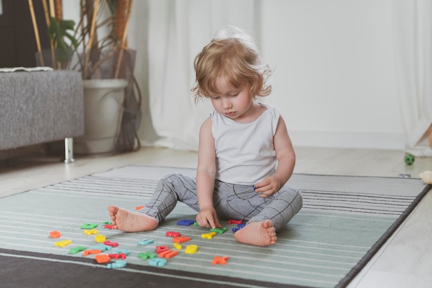 Piccolo bambino carino che gioca con le lettere giocattolo seduto sul pavimento