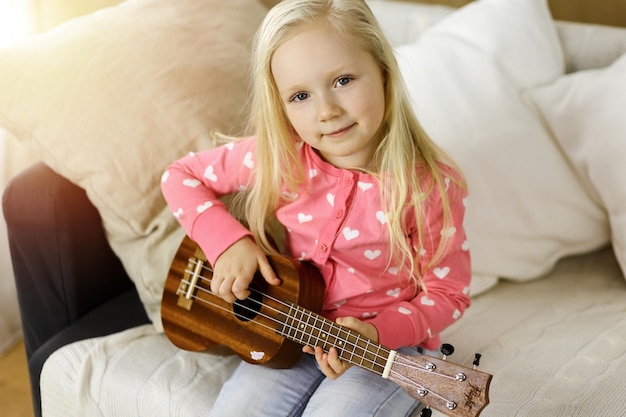 Piccolo bambino carino che suona la chitarra ukulele nella stanza soleggiata. Concetto di infanzia.