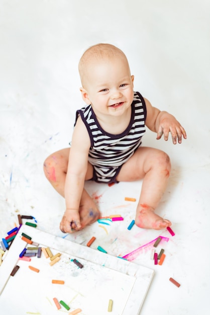 Piccolo bambino carino con creatività disegna con i pastelli a casa su un foglio di carta bianca.