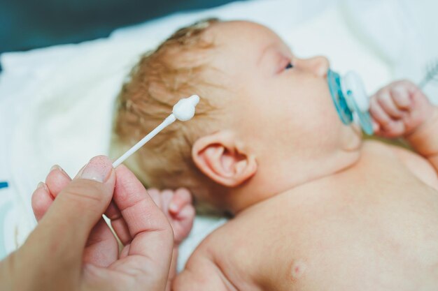 Piccolo bambino caucasico carino che guarda la telecamera mentre i suoi genitori gli puliscono le orecchie Bambino felice che si gode del bagno e dell'igiene a casa