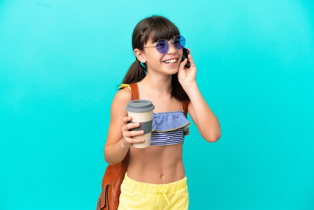 Piccolo bambino caucasico che va in spiaggia isolato su sfondo blu con in mano caffè da portare via e un cellulare