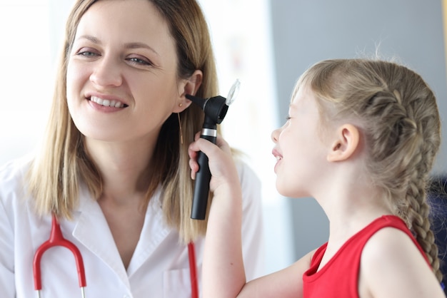 Piccolo bambino che esamina l'orecchio del medico con l'otoscopio in clinica. Diagnosi e trattamento delle malattie dell'orecchio nel concetto di bambini