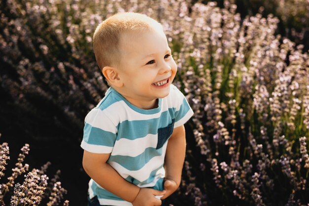 Piccolo bambino che gioca all'aperto in un campo di fiori. Ragazzino che sorride mentre distoglie lo sguardo contro il tramonto.