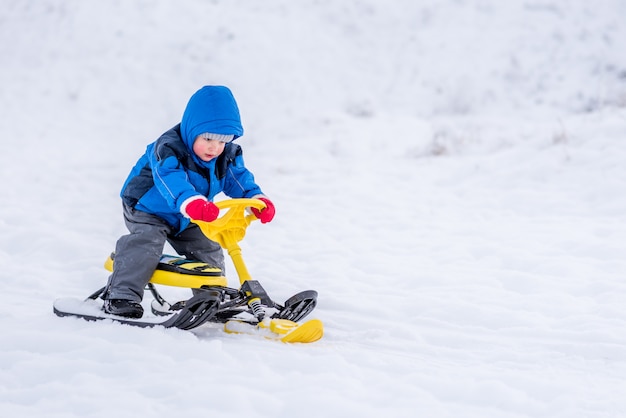 Piccolo bambino che guida un motorino di neve in inverno