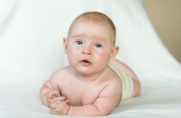 Piccolo bambino che pone sulla coperta bianca e guarda avanti