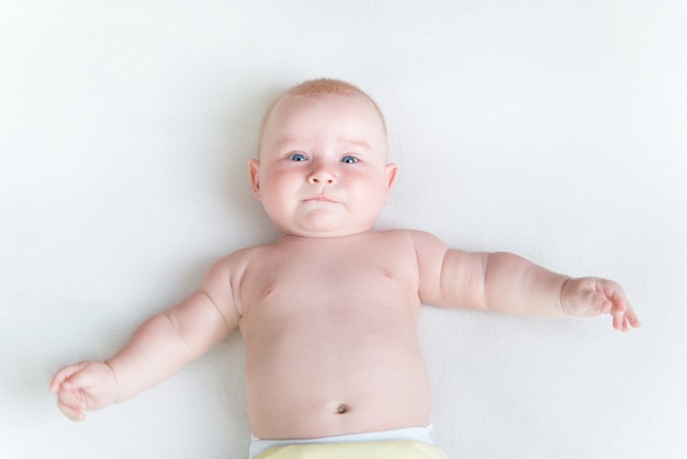 Piccolo bambino che pone sulla coperta bianca sul retro