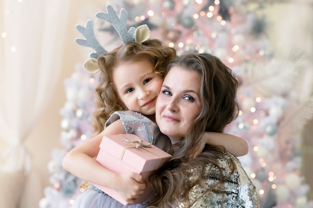 Piccolo bambino con regalo che abbraccia la madre per natale. ragazza sorridente e donna che celebrano felice anno nuovo, dando presente. famiglia felice per le vacanze, l'infanzia,