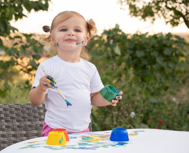 Piccolo bambino disegno con vernice e pennello. Foto di pittura ragazza piccola carina in giardino, all'aperto a casa nel cortile