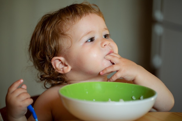 Piccolo bambino divertente in cucina che mangia con le dita dal concetto di nutrizione del bambino del piatto