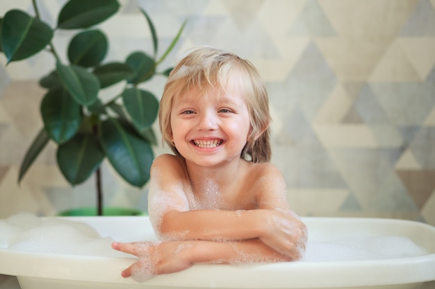 Piccolo bambino facendo un bagno in un bellissimo bagno con parete blu e fiori. Igiene dei bambini.