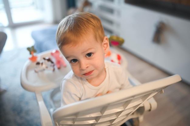 Piccolo bambino felice carino bambino biondo seduto sul seggiolone che gioca con i giocattoli per il viso del bambino