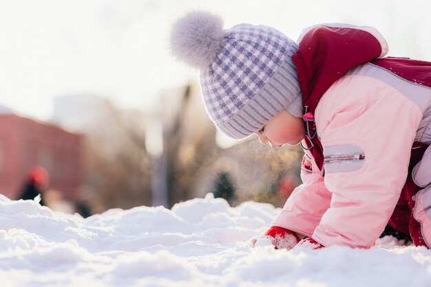 Piccolo bambino gattona sulla neve sullo sfondo di un tramonto in inverno