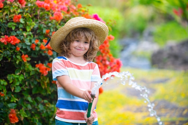Piccolo bambino giardiniere che aiuta ad innaffiare i fiori con il tubo da giardino nel lavoro stagionale del giardino estivo