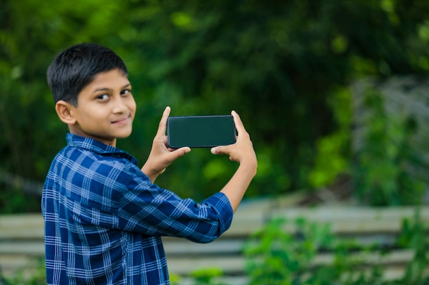 Piccolo bambino indiano sveglio che mostra smartphone con lo schermo in bianco