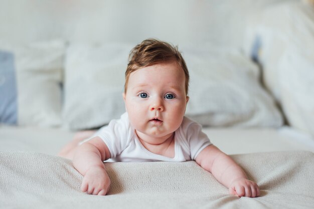 Piccolo bambino infantile che si trova sulla sua pancia sul letto bianco