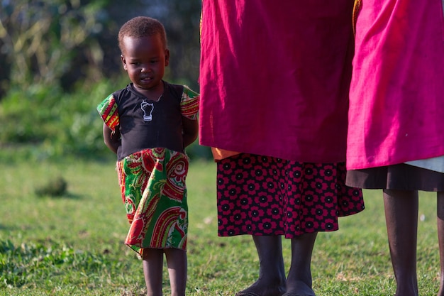 Piccolo bambino Masai che balla vicino a sua madre in abiti tradizionali. Masai Mara, Kenia