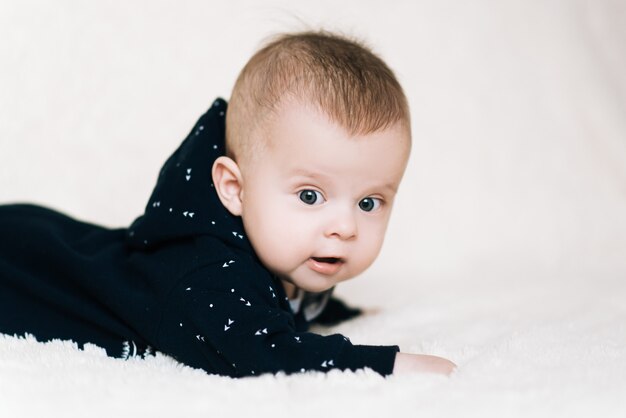 Piccolo bambino sdraiato a pancia in giù e alzando la testa un po 'sorpreso e sorridente carino, neonato